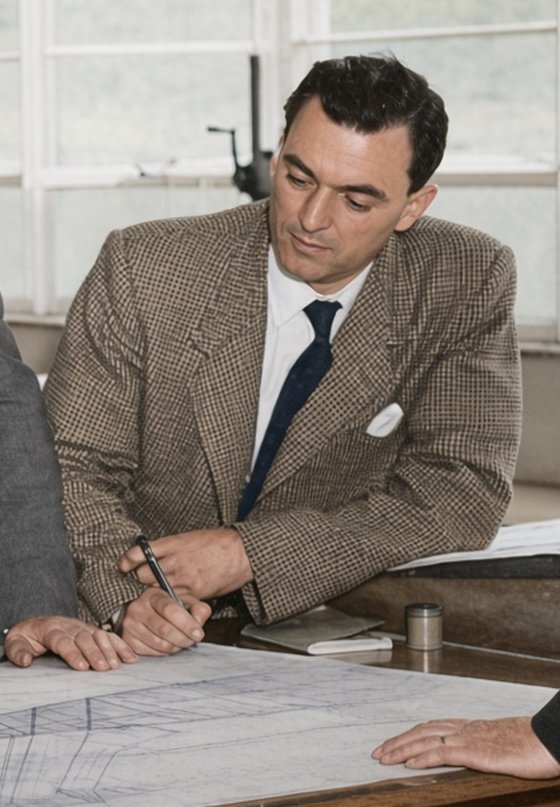 Maurice Wilmer in 1957, in a check jacket, pen in hand at a drawing table.